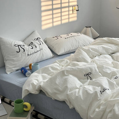 A full view of a cozy bed with a white washed cotton bedding set featuring black embroidered bows, styled in a sunlit room. - RoomDen