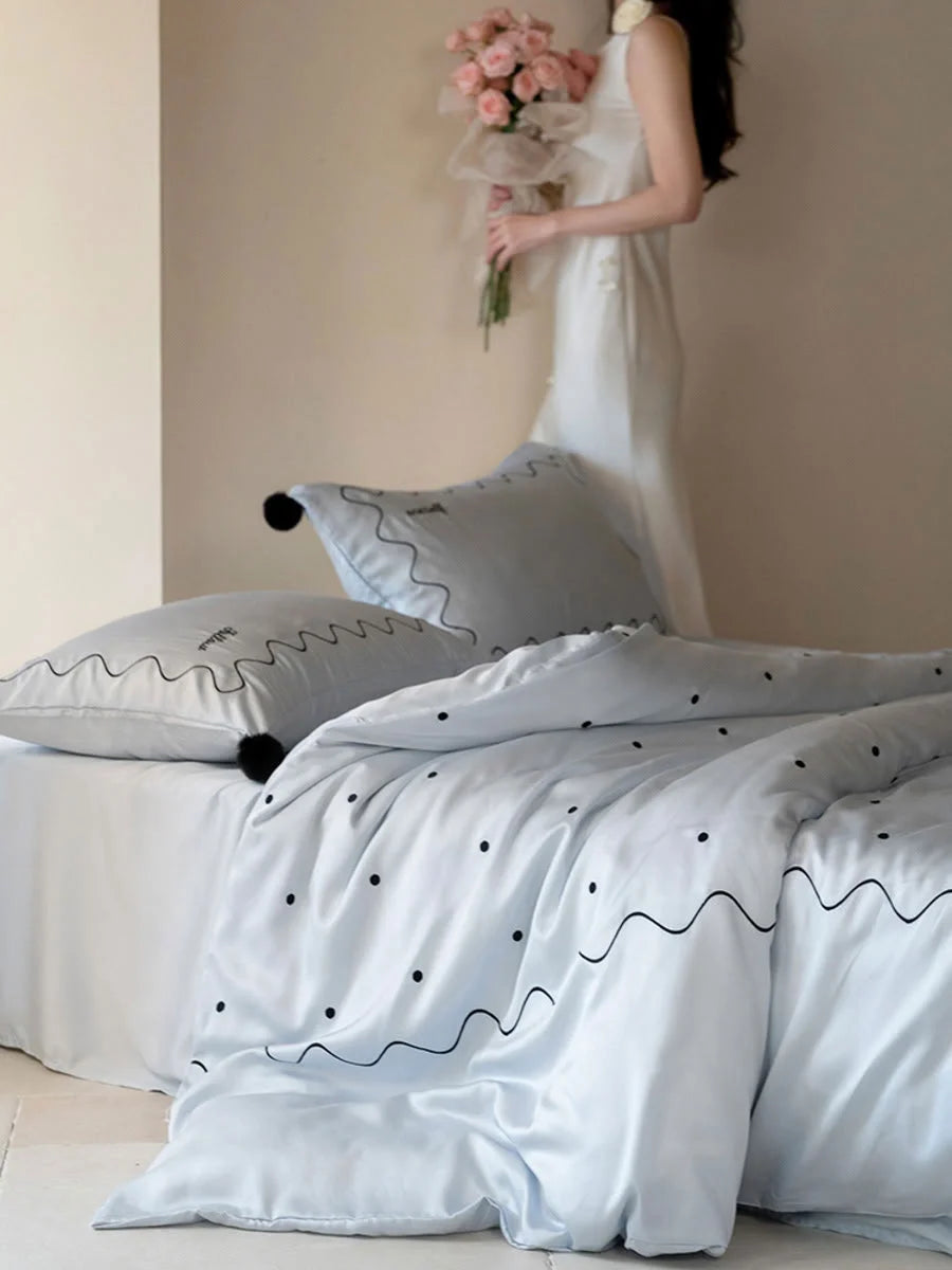 A person in a white dress holding flowers next to a bed with the Baby Blue & Black silky Tencel bedding set. - RoomDen