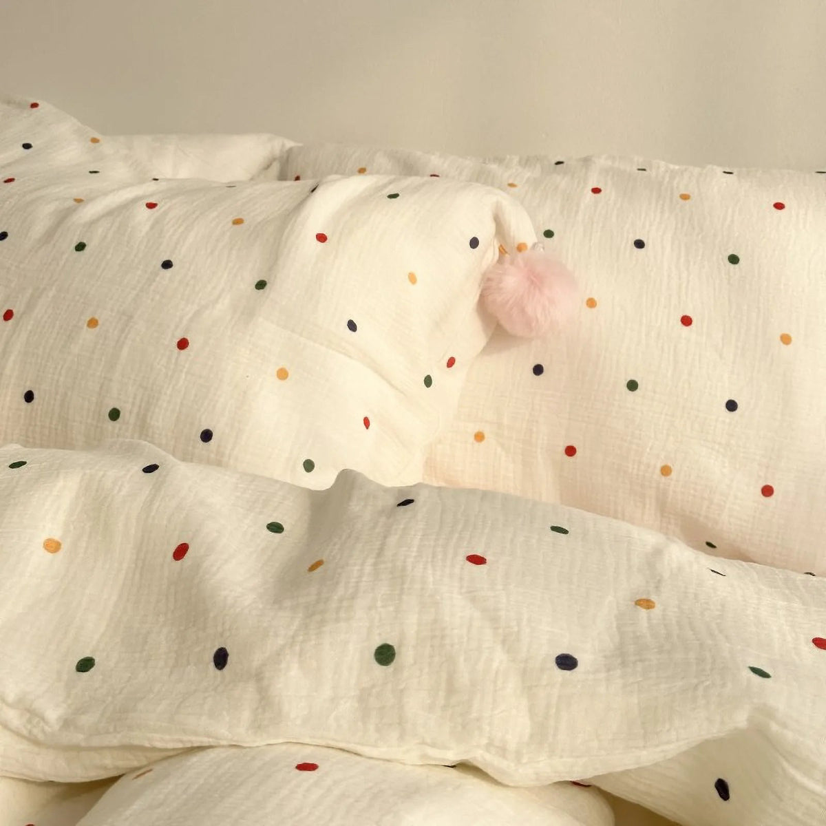 Detailed shot of the crinkled texture of the white polka dot washed cotton duvet cover, with a pink pom-pom visible. - RoomDen