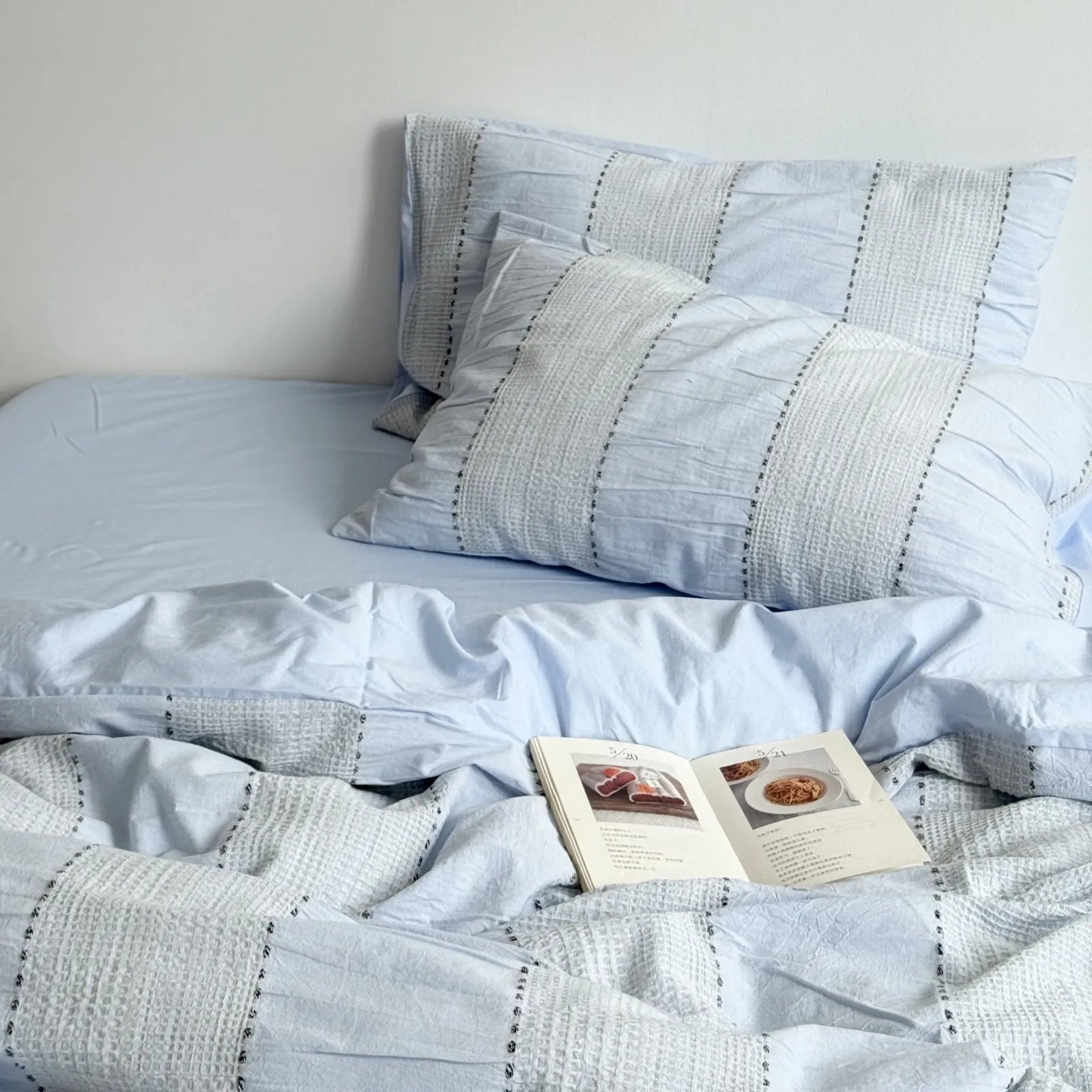 Sky Blue variant of the textured woven stripe bedding set, styled with an open book. - RoomDen