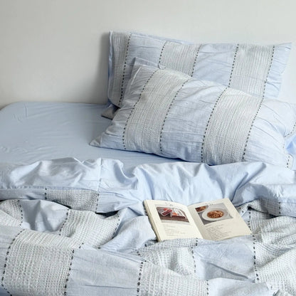 Sky Blue variant of the textured woven stripe bedding set, styled with an open book. - RoomDen