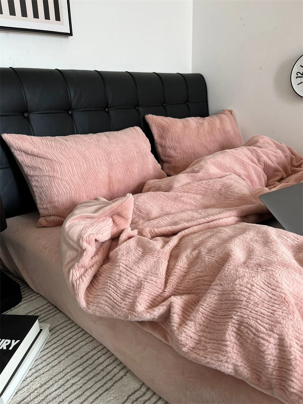 A cozy, unmade bed with a Blush Pink ruched fleece bedding set, laptop, and books on a nightstand. - RoomDen