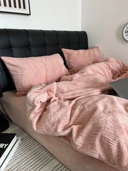 A cozy, unmade bed with a Blush Pink ruched fleece bedding set, laptop, and books on a nightstand. - RoomDen