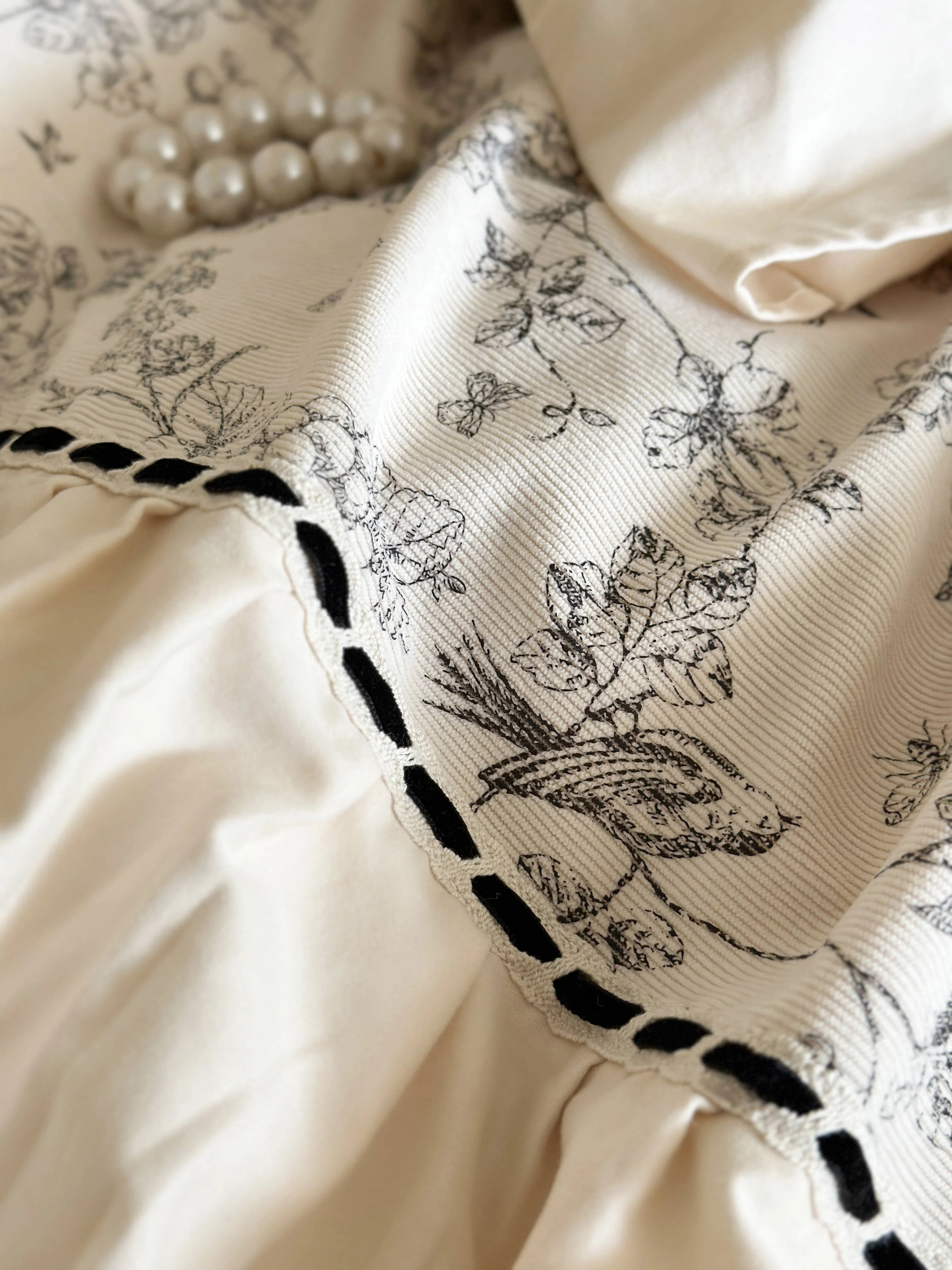 Detailed close-up of the botanical toile fabric and black stitched trim on the Cream Toile bedding. - RoomDen