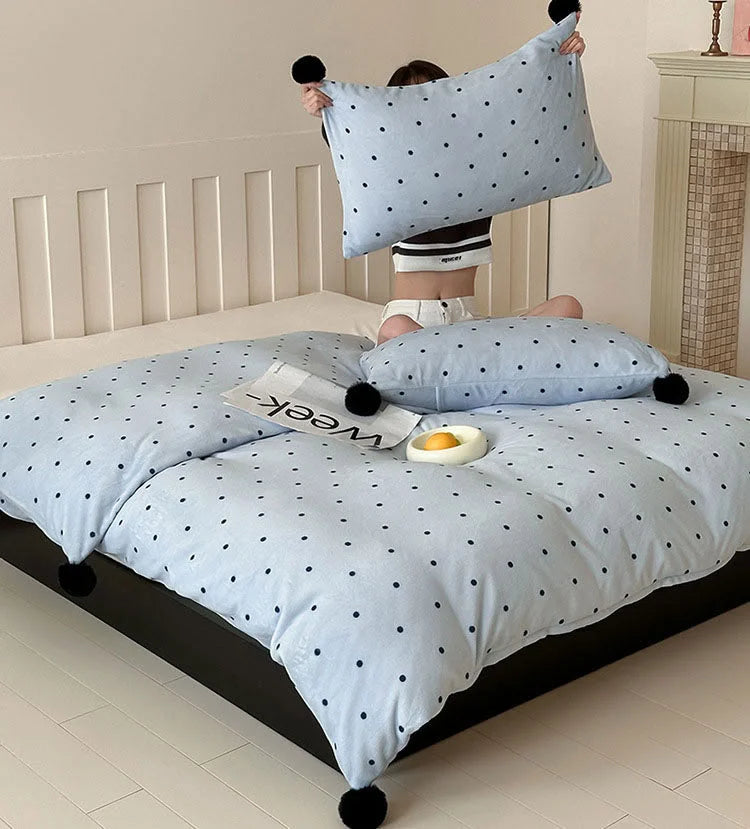 A person sitting on a bed with the Baby Blue Polka Dot Pom Pom Velvet Bedding Set, holding up a pillowcase. - RoomDen