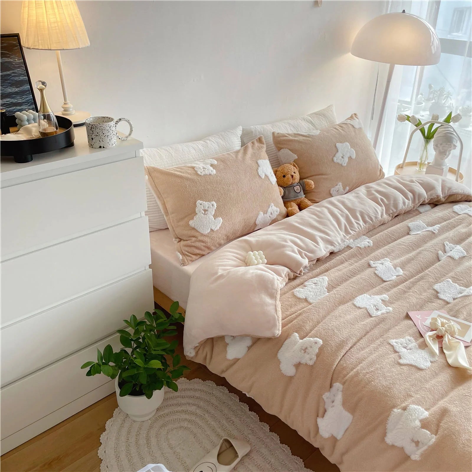 The creamy beige teddy bear bedding set styled on a bed with a teddy bear plush toy and a plant nearby. - RoomDen
