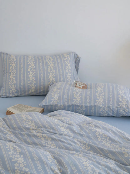 Close-up of the cornflower blue floral stripe pillowcases and duvet cover, with an open book and perfume bottle. - RoomDen