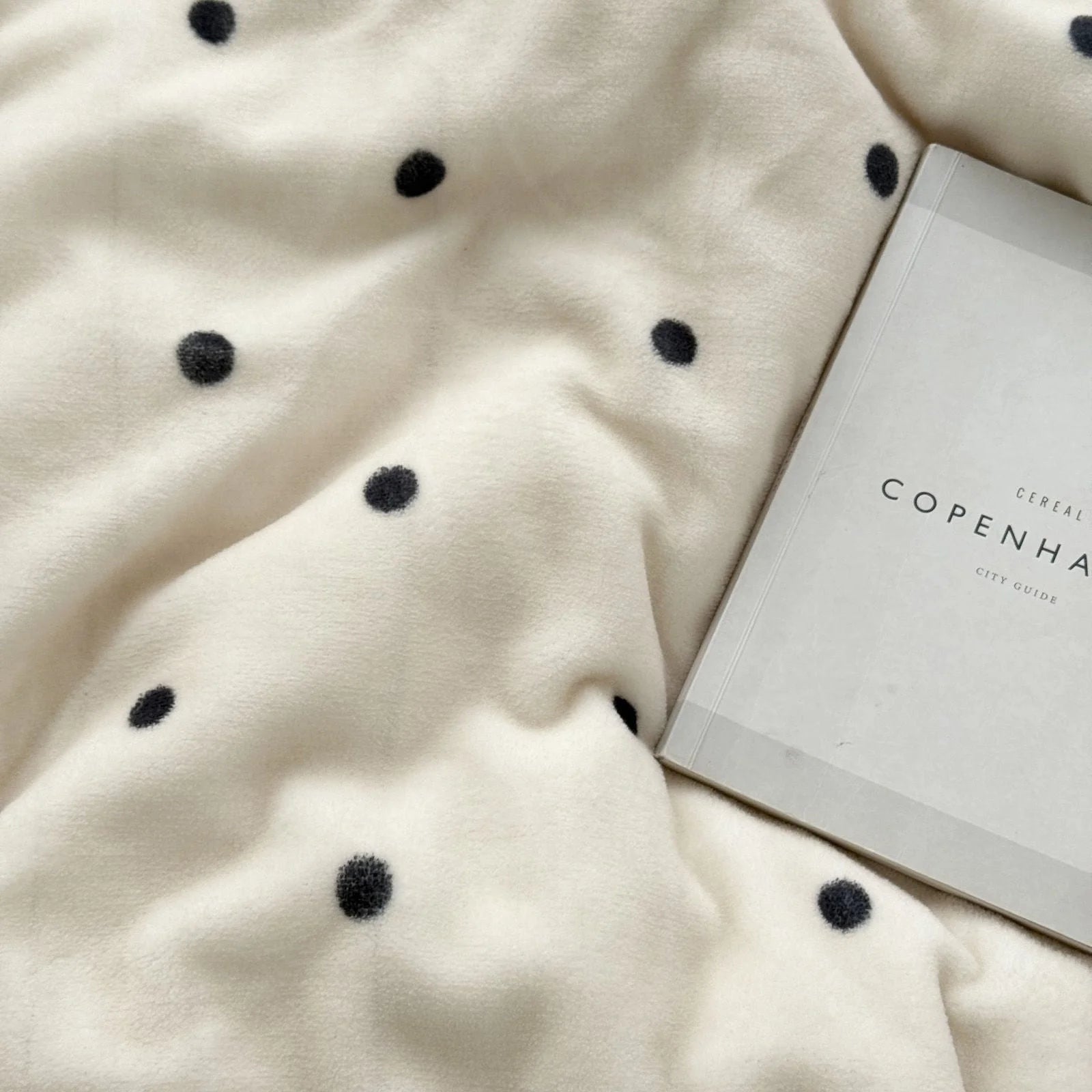 A 'Copenhagen' city guide book resting on the soft Creamy White Polka Dot Flannel Fleece duvet cover.