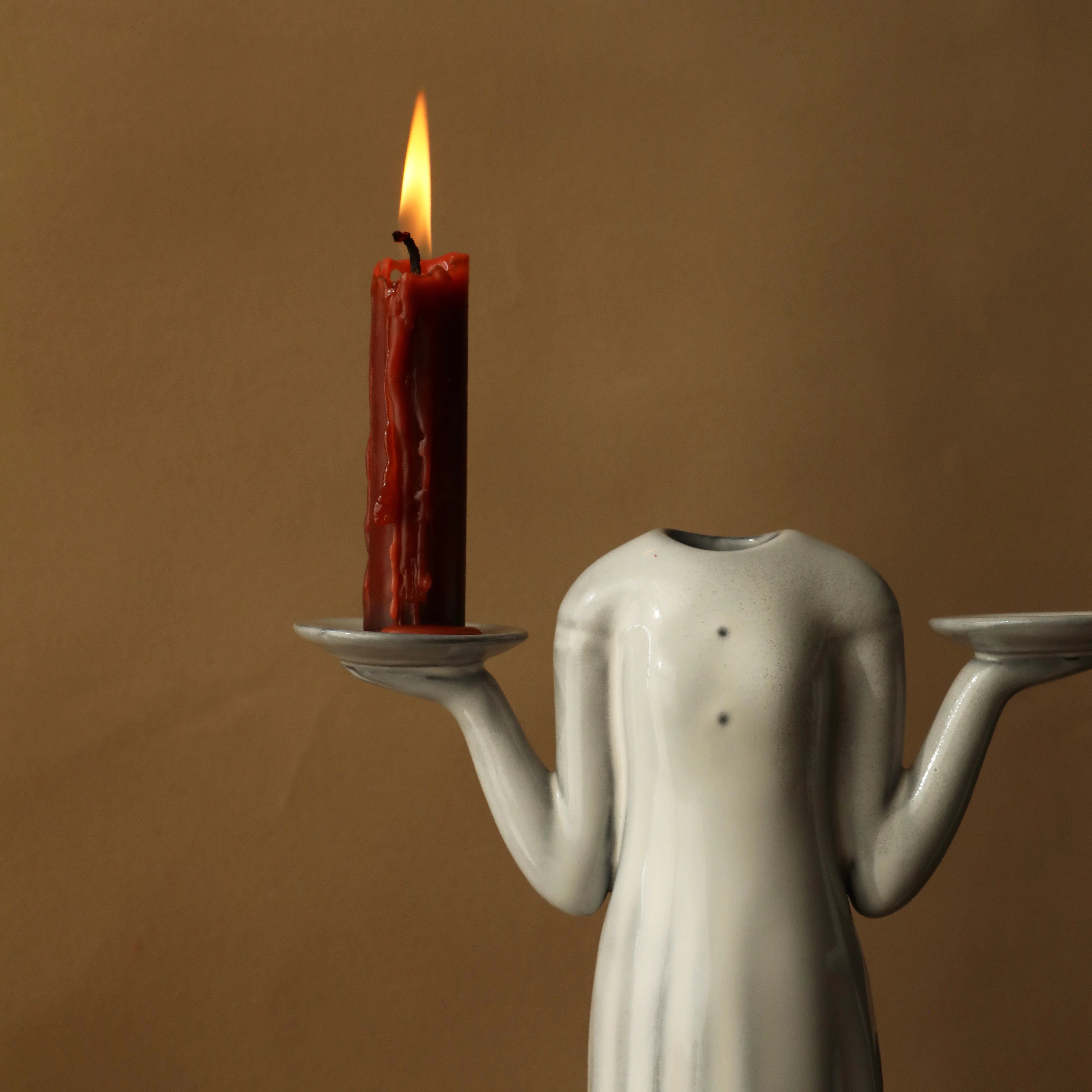 The tall female figure vase being used as a candle holder with a lit red candle. - RoomDen