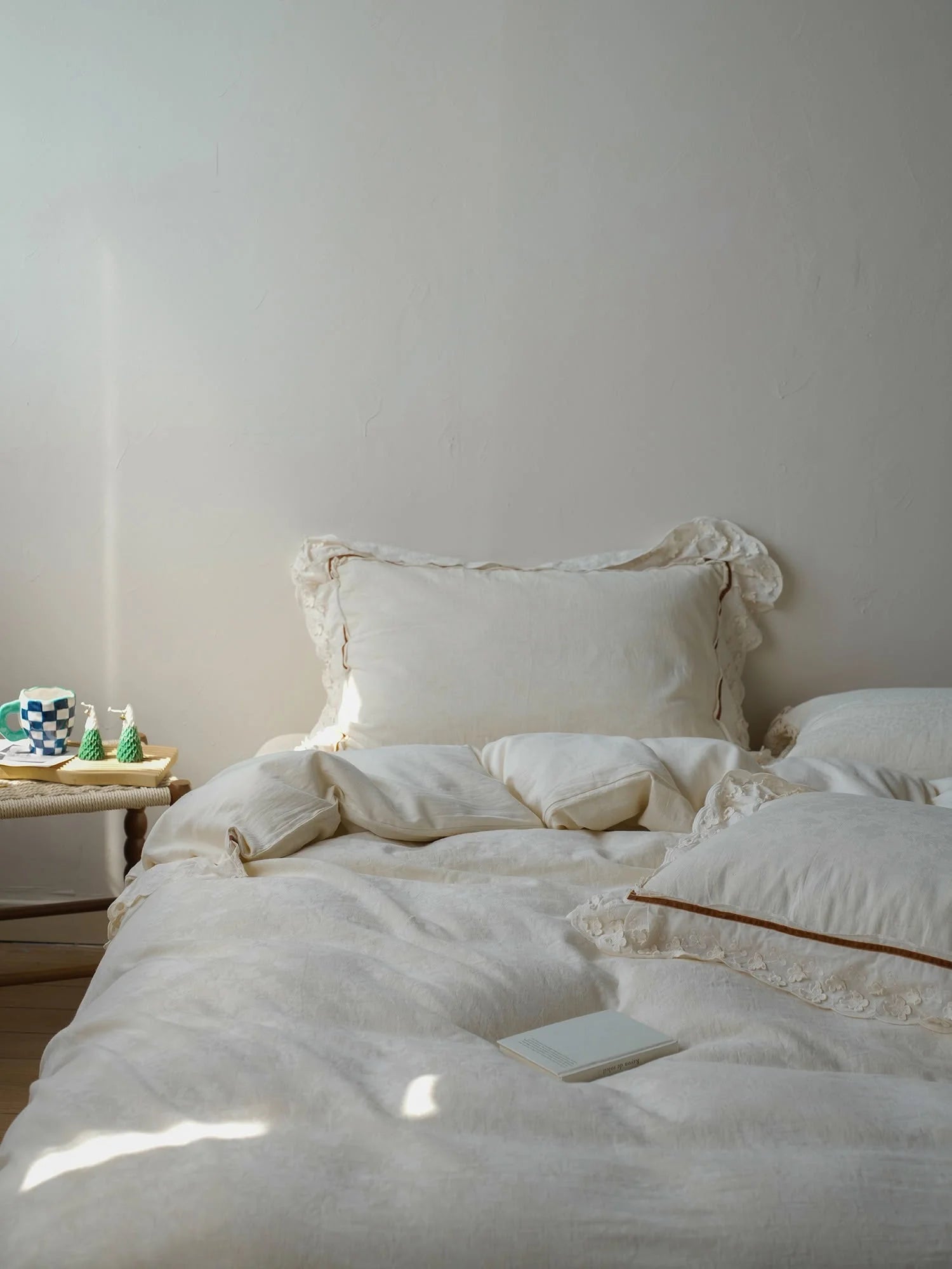 Sunbeam falling across the creamy white linen duvet cover, highlighting its soft texture next to a small side table. - RoomDen