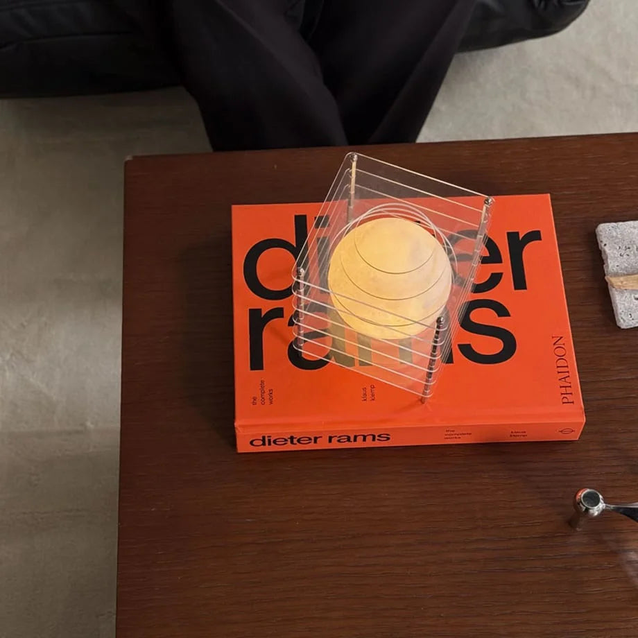 Overhead shot of the Crystal Clear Caged Lamp on an orange book, showing its transparent design - RoomDen