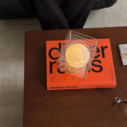 Overhead shot of the Crystal Clear Caged Lamp on an orange book, showing its transparent design - RoomDen