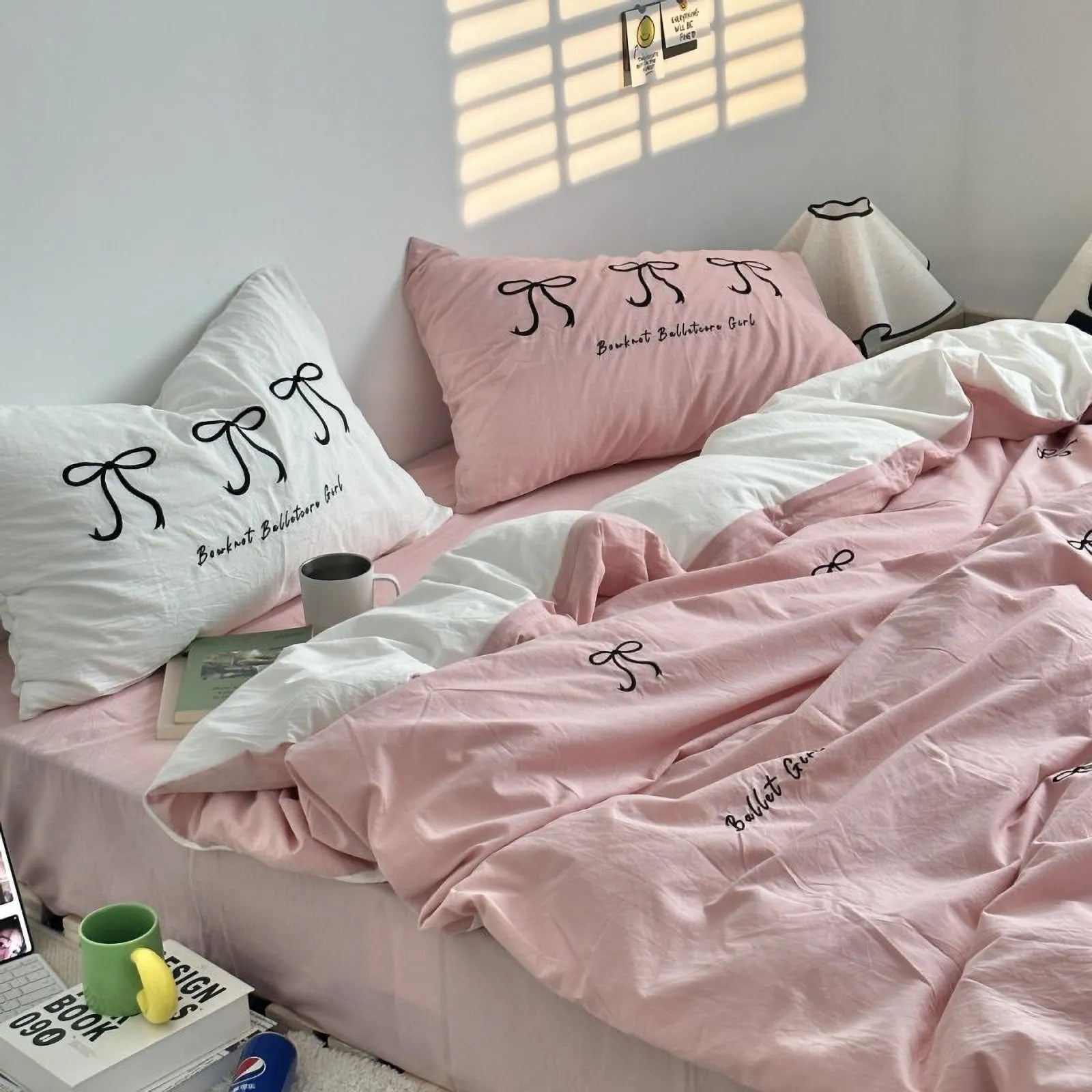 A pink washed cotton bedding set with black embroidered bows, shown in a cozy, sunlit bedroom setting. - RoomDen
