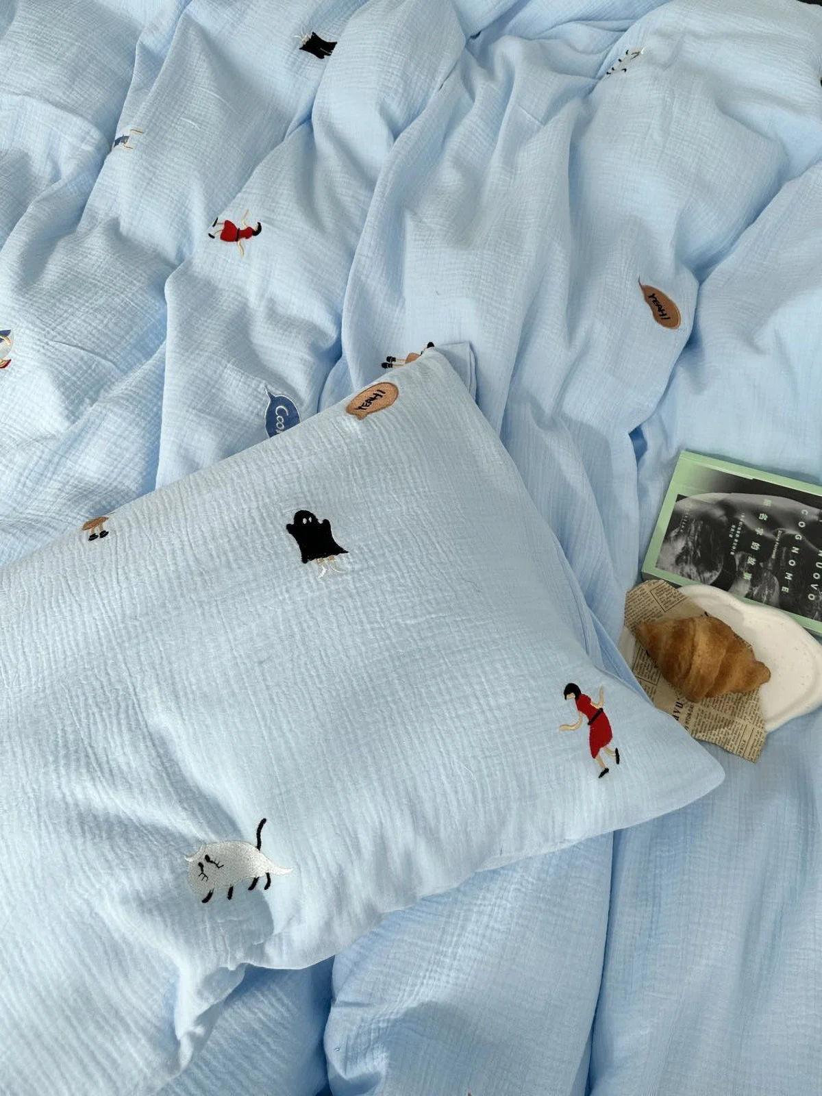 A top-down view of the sky blue bedding set, showcasing the scattered embroidered characters and soft texture.