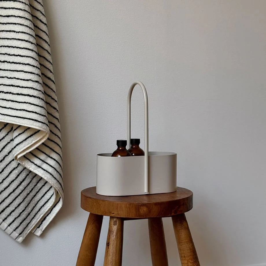 Angled view of the beige metal organizer caddy with a striped towel hanging in the background. - RoomDen