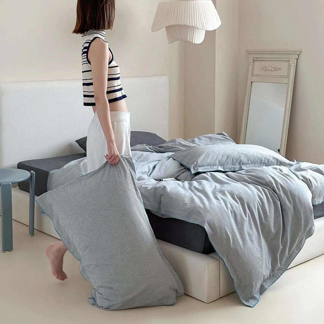 A woman arranging a pillow on the Dark Grey & Blue Pinstripe Washed Cotton Bedding Set.