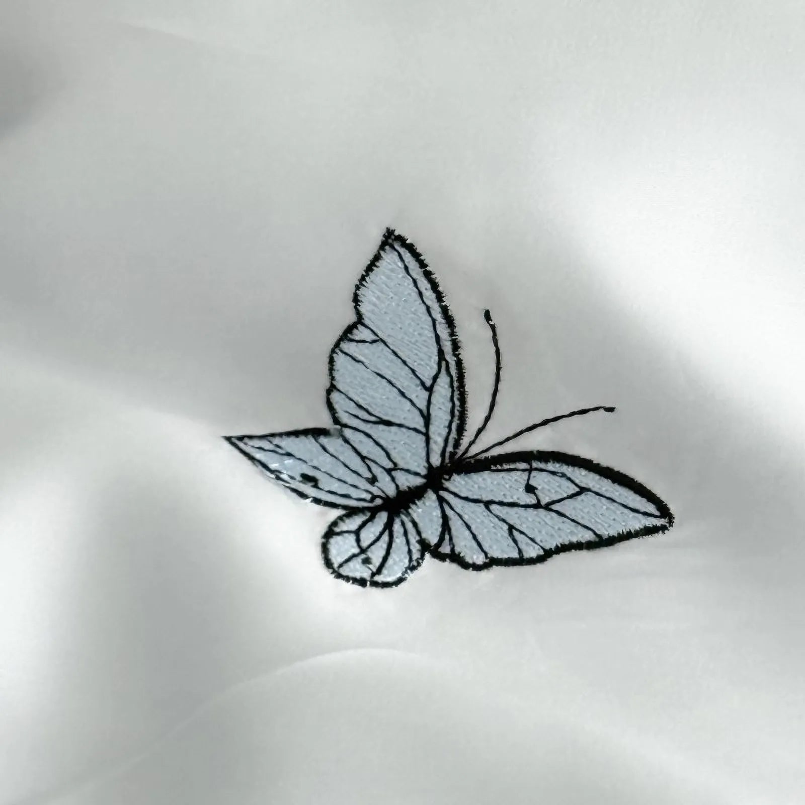 Macro close-up of a single embroidered blue butterfly on the smooth, silky Cloud Blue Tencel fabric.