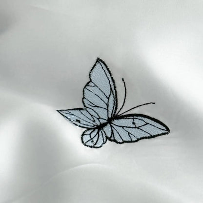 Macro close-up of a single embroidered blue butterfly on the smooth, silky Cloud Blue Tencel fabric.