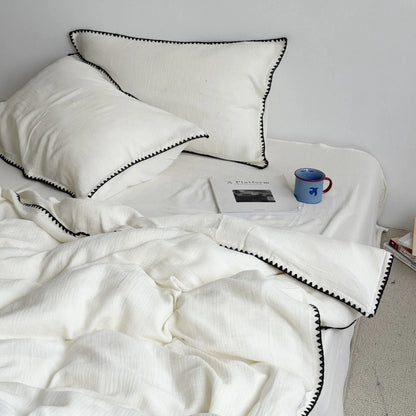 Cream white washed cotton bedding set with black embroidered edge, styled on a bed with a book and mug. - RoomDen