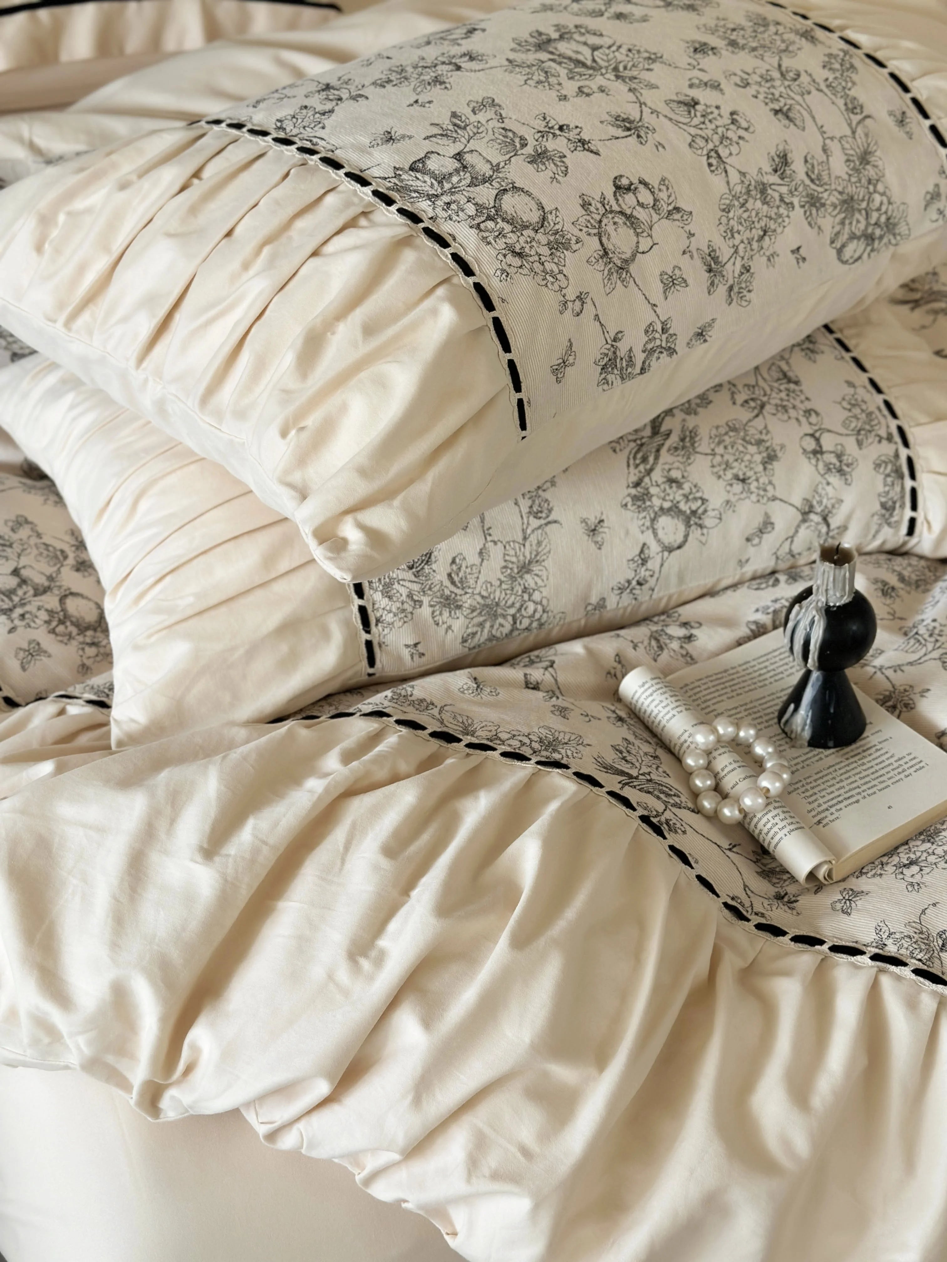 Close-up of the ruched pillows on the Cream Toile bedding, with a book and pearls for a vintage touch. - RoomDen