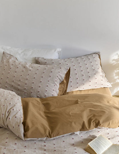 The Ditsy Cherry Washed Cotton Bedding Set on a bed, showing the reversible mocha brown side folded over - RoomDen.