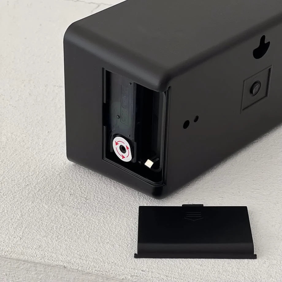 Back of the black flip clock with the battery compartment open. - RoomDen