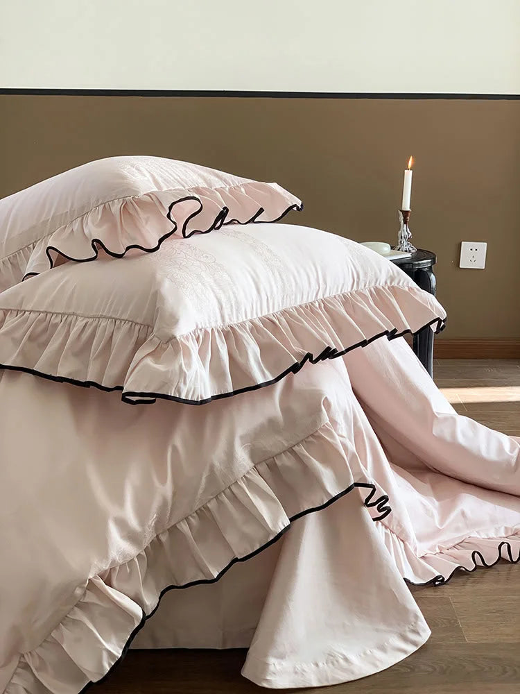 Close-up view of the stacked Blush Pink ruffled pillows, emphasizing the black trim detail - RoomDen.