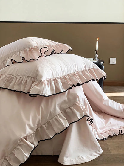 Close-up view of the stacked Blush Pink ruffled pillows, emphasizing the black trim detail - RoomDen.