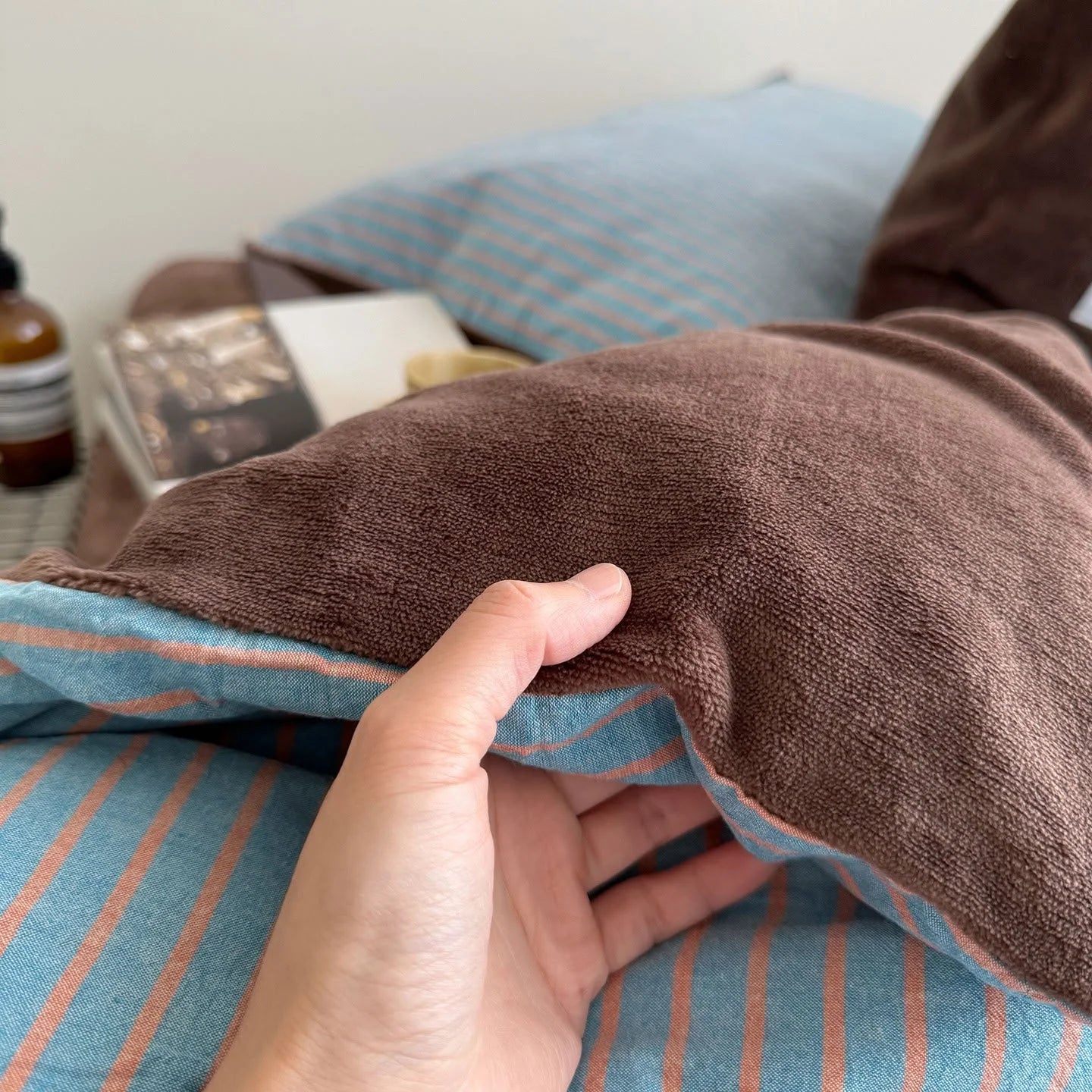 Close-up of a hand touching the soft brown fleece, with the blue striped reverse visible.