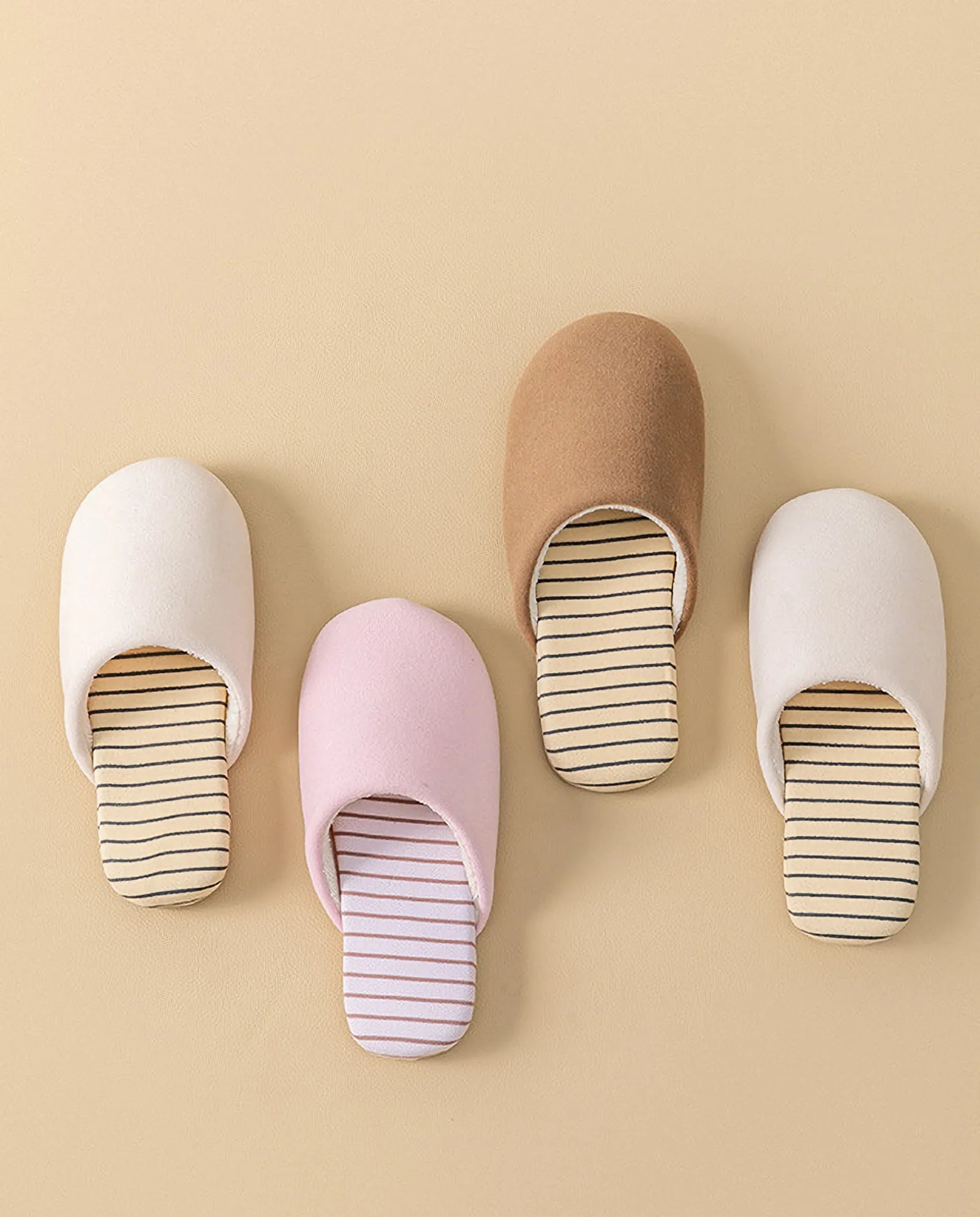 Top view of four pairs of cotton house slippers in white pink brown and beige arranged neatly