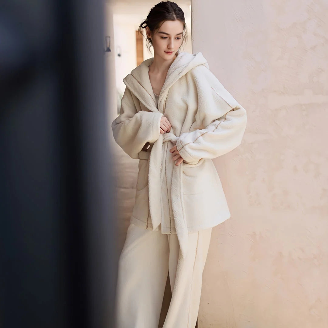 Model tying the belt of her creamy white plush fleece pajama set in a softly lit hallway - RoomDen.
