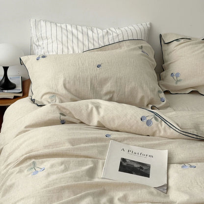 Top-down view of the cozy blueberry embroidered linen duvet cover with a book resting on it. - RoomDen