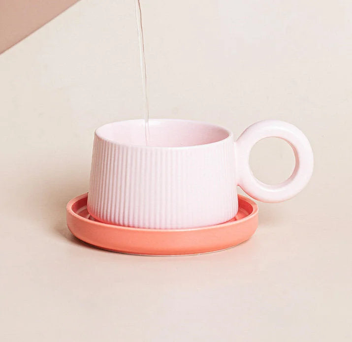 A lifestyle shot of the pink ribbed ceramic mug with a coral saucer, with water being poured into it. - RoomDen