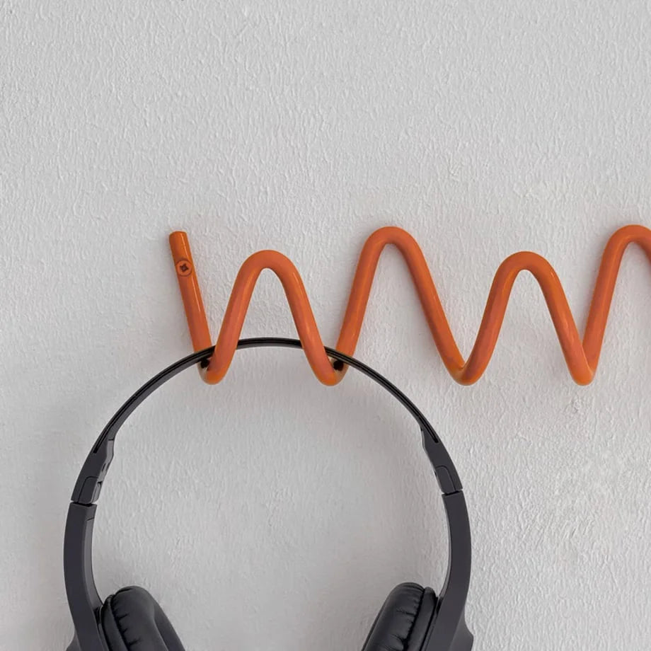 Top-down close-up view of the Wavy Coil Metal Wall Hook with headphones resting in a coil. - RoomDen
