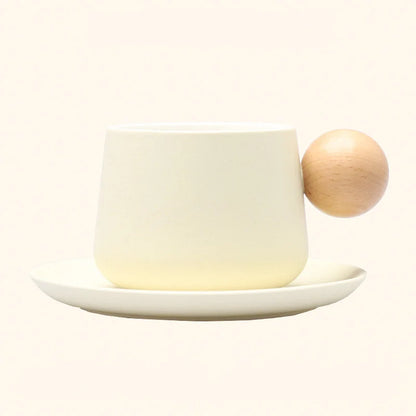 A studio shot of the Creamy White Frosted Ceramic Mug and Saucer Set with a wooden ball handle. - RoomDen