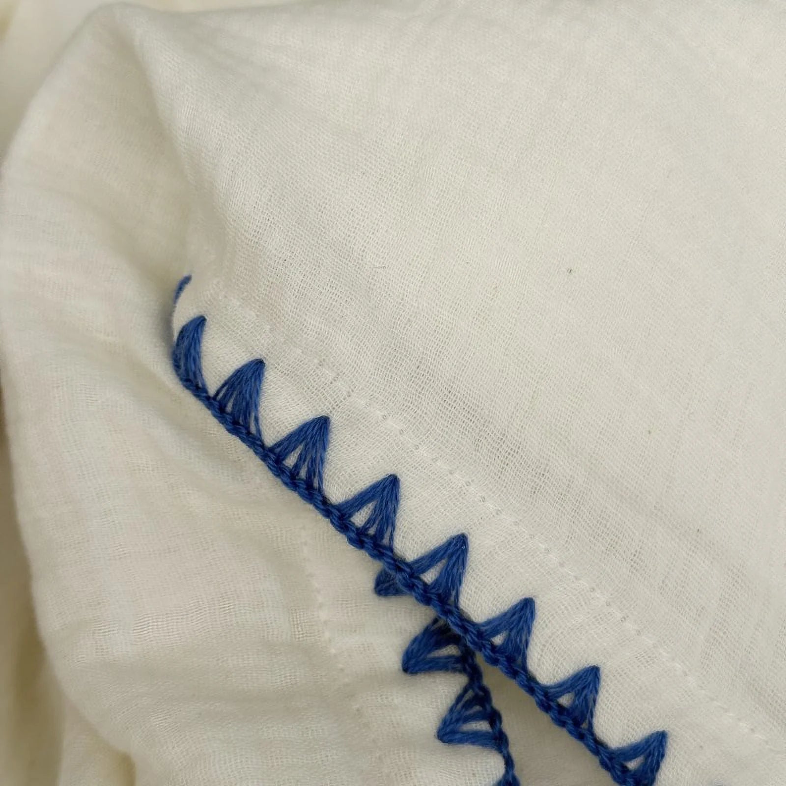 Close-up of the blue triangular embroidered trim on a textured cream white washed cotton fabric.
