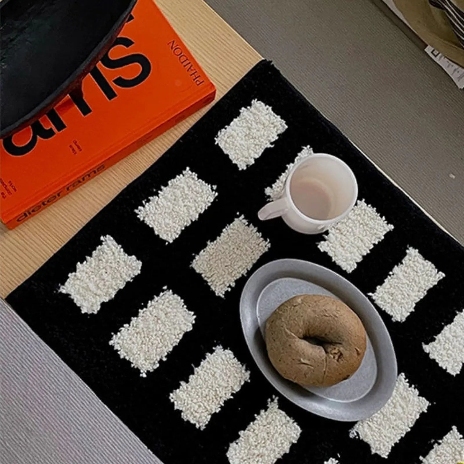 Small black and white textured rug styled on a table with an orange book and coffee - RoomDen