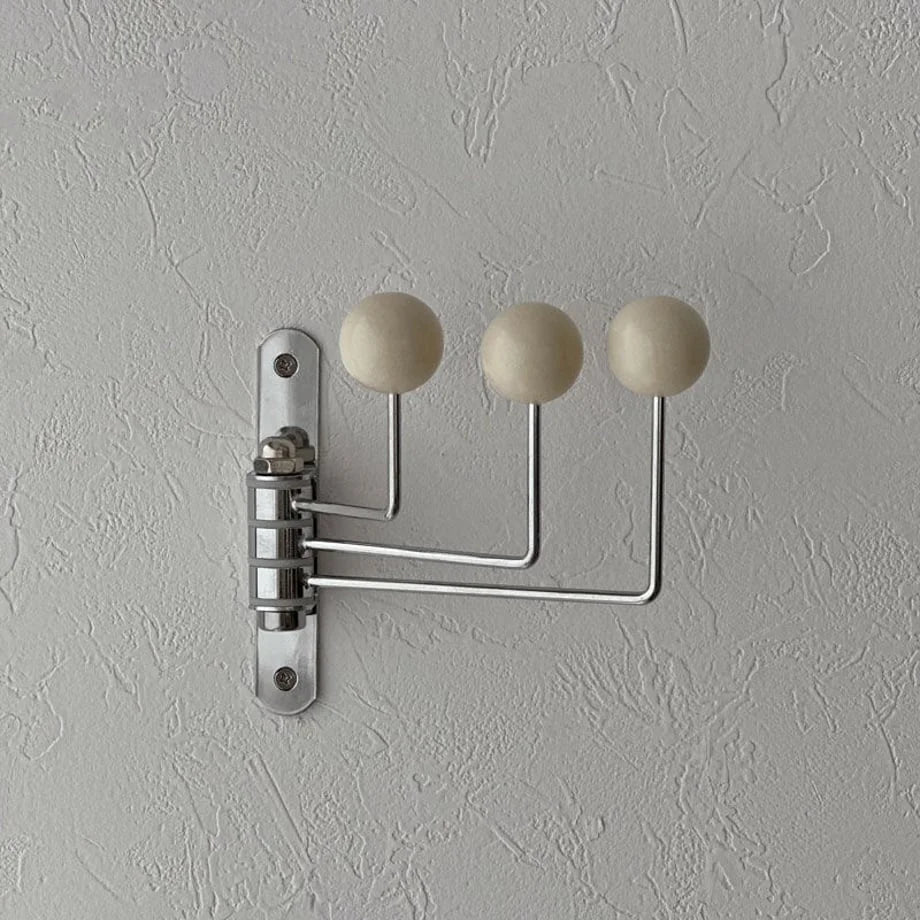 Detailed shot of the cream swivel wall hook's mounting plate and hinge on a grey textured wall - RoomDen.