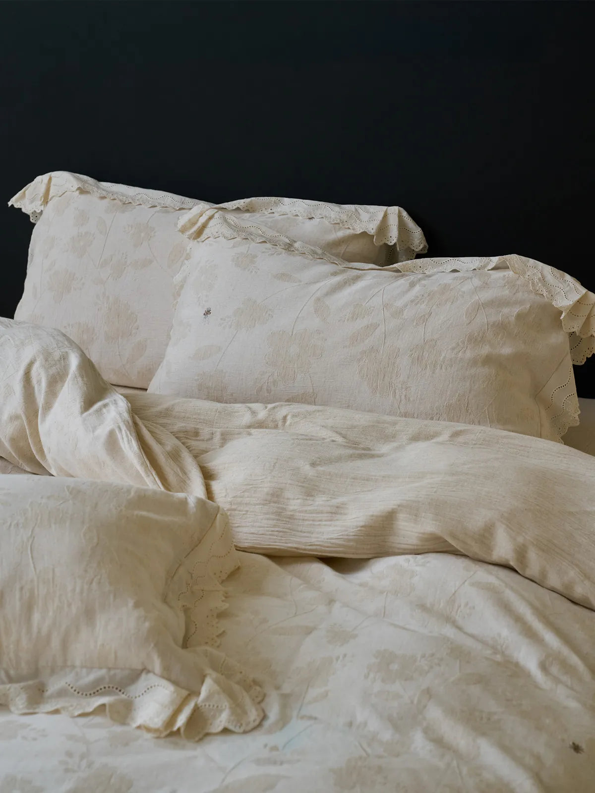 Angled view of a rumpled Antique White linen duvet cover and matching ruffle-trimmed pillowcases on a bed - RoomDen