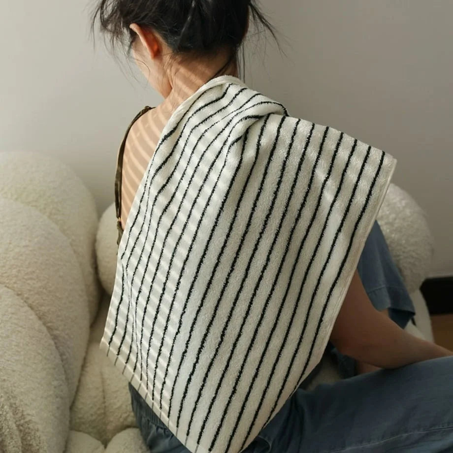 A woman with a striped cotton towel draped over her shoulder, sitting on a cozy bouclé sofa.