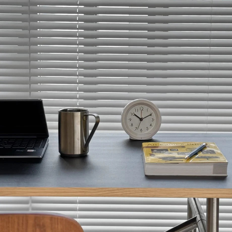 The white analog alarm clock in a bright, modern office setting next to a laptop and mug. - RoomDen