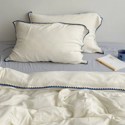 Full view of the cream white and blue embroidered washed cotton bedding set styled on a bed with a book. - RoomDen