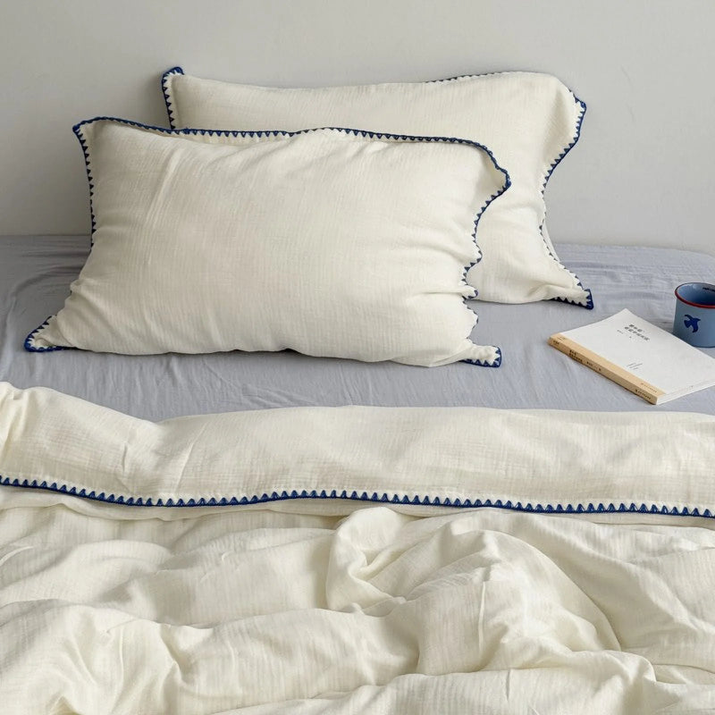Full view of the cream white and blue embroidered washed cotton set styled on a bed with a book, blue used only at the edge. - RoomDen