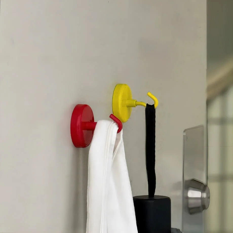Red and yellow magnetic hooks holding towels on a light-colored wall near a door - RoomDen