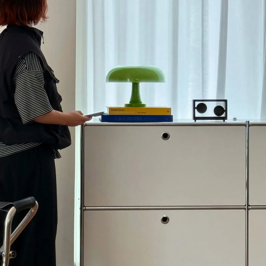 A lime green mushroom lamp on a stack of books atop a white modular cabinet - RoomDen.