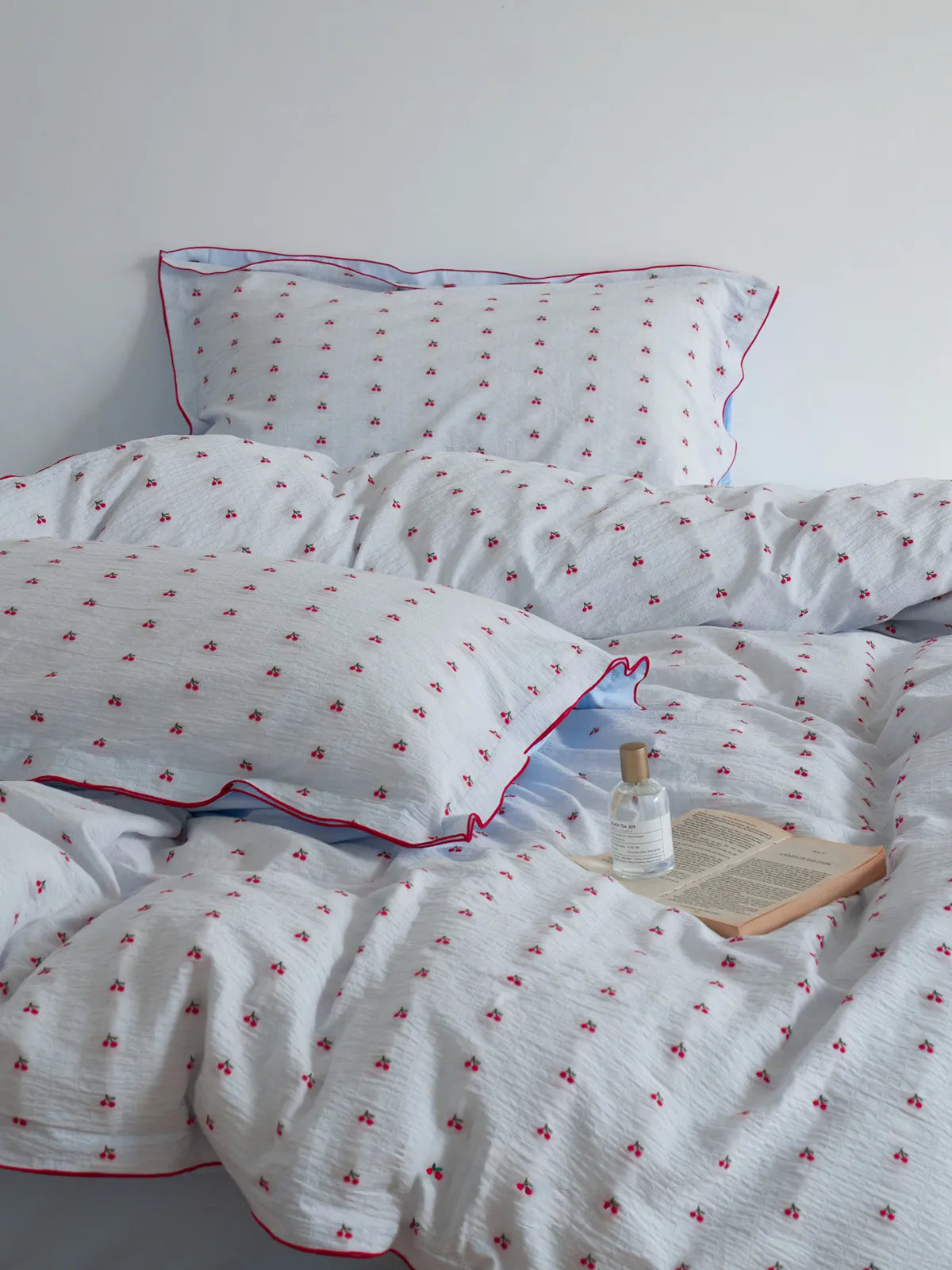 Full view of the Textured Cherry Print Cotton Bedding Set, styled with a book and perfume bottle. - RoomDen
