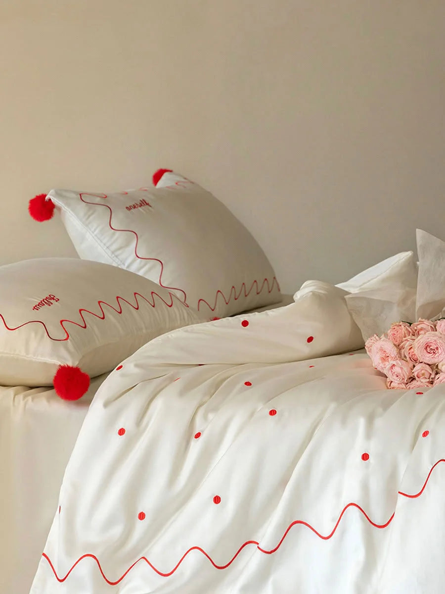 Close-up of the Creamy White & Red embroidered Tencel duvet cover and pillowcases with red pom poms. - RoomDen