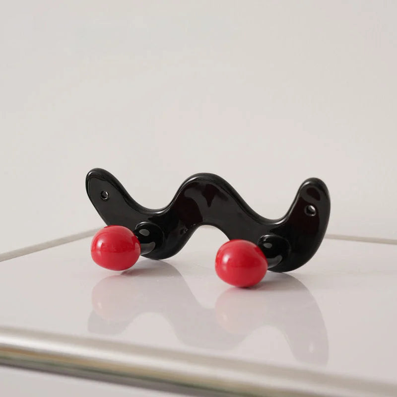 Two-hook wavy black ceramic wall hook with red balls on a white surface.