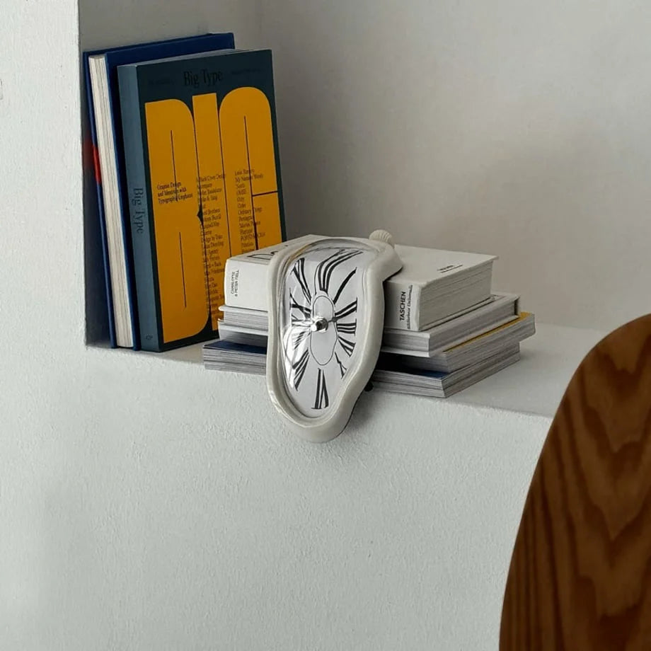 White Surrealist Melting Clock resting on a stack of design books on a white shelf.