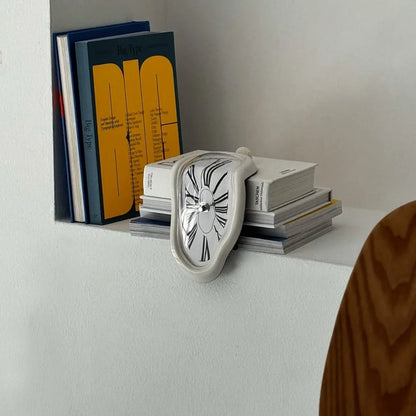 White Surrealist Melting Clock resting on a stack of design books on a white shelf.